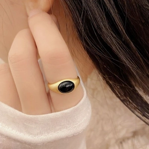 Close-up of a matte gold signet ring with an oval black agate stone on a hand