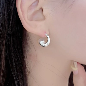 Gros plan détaillé d'une boucle d'oreille en argent massif en forme de C avec texture spirale