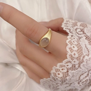 Elegant gold ring with oval chalcedony gemstone worn on finger against white satin