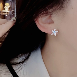 Detail of flower stud earrings with white petals and a blue zircon center on model's ear