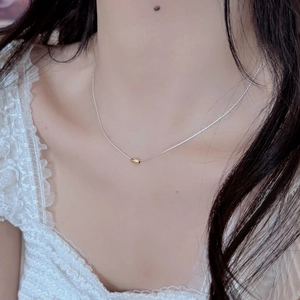 Close-up of minimalist silver chain necklace featuring a polished gold bean pendant