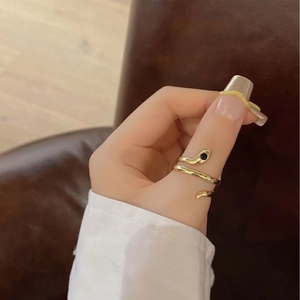 Detail of adjustable gold snake ring with black gemstone worn on thumb over leather