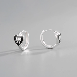 Macro detail of S925 sterling silver heart earrings with black enamel and white bow