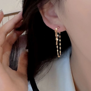 Detail of elegant gold tassel earrings with flat oval chain links on model ear