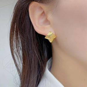 Détail macro d'un clou d'oreille carré doré avec texture quadrillée fine porté à l'oreille