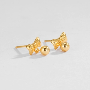 Detail of polished gold bow stud earrings with small round bead pendants on white backdrop