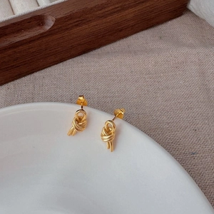 Minimalist double-layered knotted gold stud earrings on a white plate with linen background