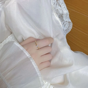 Dettaglio anello dorato intrecciato con zircone rettangolare sulla mano di donna