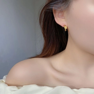 Detail of gold knotted double-line stud earring worn by a model on a grey background