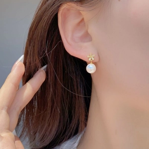 Detailed close-up of a flower-shaped gold earring with zircon inlay and round white pearl