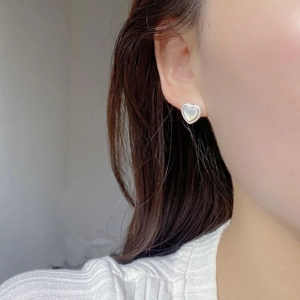 Close-up of heart-shaped white mother of pearl stud earrings with twisted silver edges