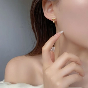 Close-up of a gold bow and bead stud earring worn by a model in a minimalist style
