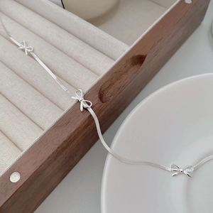 Close-up of minimalist S925 sterling silver bow necklace on a wooden jewelry box