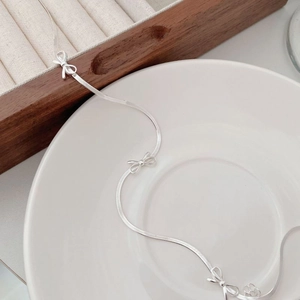 Detailed macro of S925 sterling silver bow necklace with flat snake chain on tray