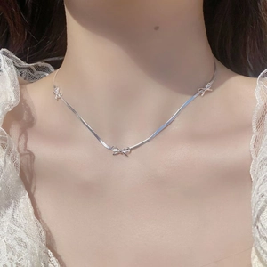 Close-up of S925 silver bow necklace on a snake chain against a lace collar