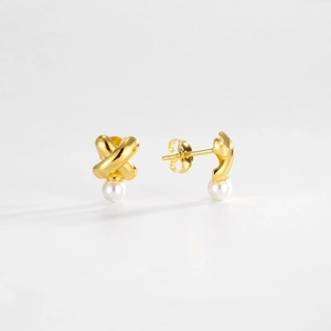 Macro detail of gold-plated cross earrings with white round pearls on white surface