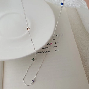 Macro view of a silver S925 necklace with five colorful round gemstones on a white dish