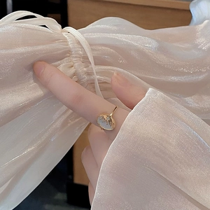 Gros plan d'une bague dorée avec motif soleil et nacre blanche portée par un mannequin