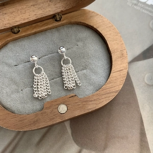 Macro detail of S925 sterling silver tassel stud earrings inside a wooden jewelry box