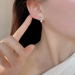 Macro detail of S925 sterling silver cross earrings with a round white pearl on earlobe