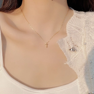 Minimalist gold cross necklace worn by model on pearl knit sweater for elegant style