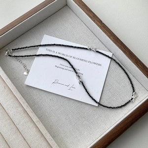 Detail view of S925 silver bow necklace with black faceted beads on a linen display