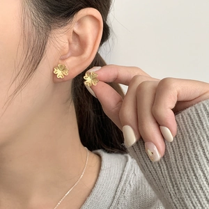 Détail des boucles d'oreilles trèfle dorées avec texture filigranée sur l'oreille