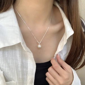 Detail of elegant white round pearl pendant on thin silver chain worn with a linen shirt