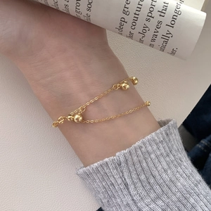 Gros plan d'un bracelet double chaîne dorée avec cinq perles lisses porté au poignet