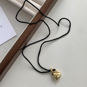 Détail d'un pendentif cœur doré poli avec un cordon noir réglable sur un plateau