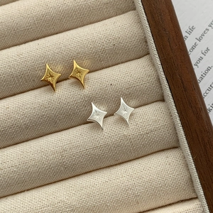 Close-up of gold and silver S925 star studs on beige velvet jewelry tray