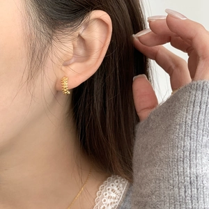Detailed view of textured gold hoop earring with geometric patterns on model ear