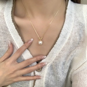 Close-up of a gold necklace with a white synthetic pearl pendant on a female model