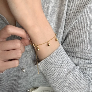 Détail d'un bracelet ajustable en métal doré avec trois perles polies porté au poignet délicat