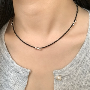 Detail view of S925 silver bow necklace with black faceted beads on model neckline