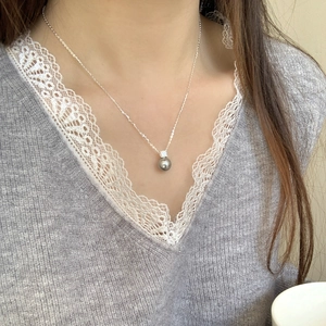 Detail of a dark gray pearl pendant with zircon on a silver chain worn by a model