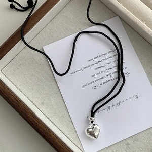 Gros plan d'un pendentif cœur en argent poli sur cordon noir dans un plateau en bois