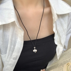 Pendentif coeur en argent minimaliste avec cordon noir porté sur une chemise en lin