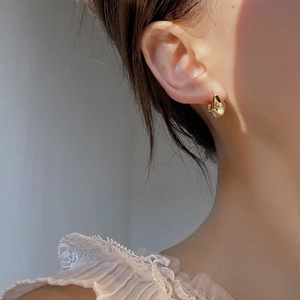Close-up of golden irregular geometric hoop earrings on ear with lace clothing