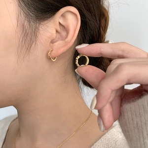 Nahaufnahme kleiner goldener Creolen mit Blattstruktur am Ohr eines Modells