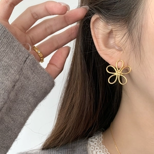 Detailed view of hollow gold floral stud earrings worn by a model in a minimalist style