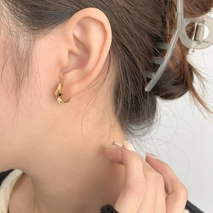 Close-up of minimalist gold star-shaped hoop earring worn on woman's earlobe