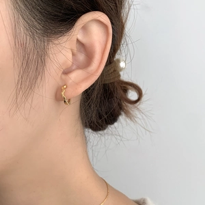 Detailansicht goldener gedrehter Creolen am Ohr mit elegantem strukturiertem Design