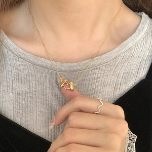 Close-up of a gold hand-heart pendant necklace with a textured silver ring on model