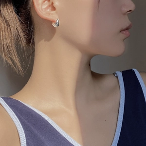 Detail of silver drop-shaped C-style earring on model with sharp sunlight and shadow