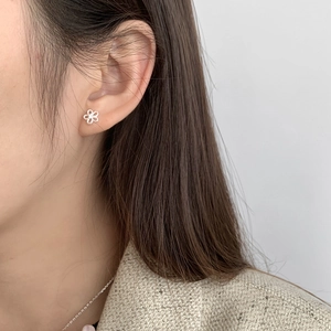 Detail of a minimalist S925 sterling silver hollow flower stud earring on a model ear
