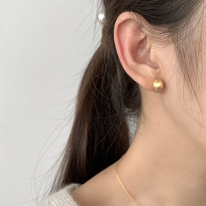 Close-up of minimalist brushed gold bean earrings worn by a model in a natural setting