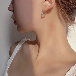 Close-up of model wearing minimalist gold geometric trapezoid earrings in natural sunlight