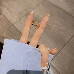 Close-up of a wide hollow gold ring with repeated B-letter design worn on a finger