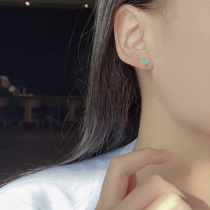 Close-up of green round smiley face stud earrings worn by a model in silver
